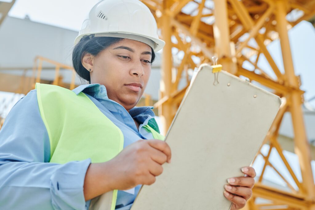 Woman in hardhat appears stressed while reviewing clipboard