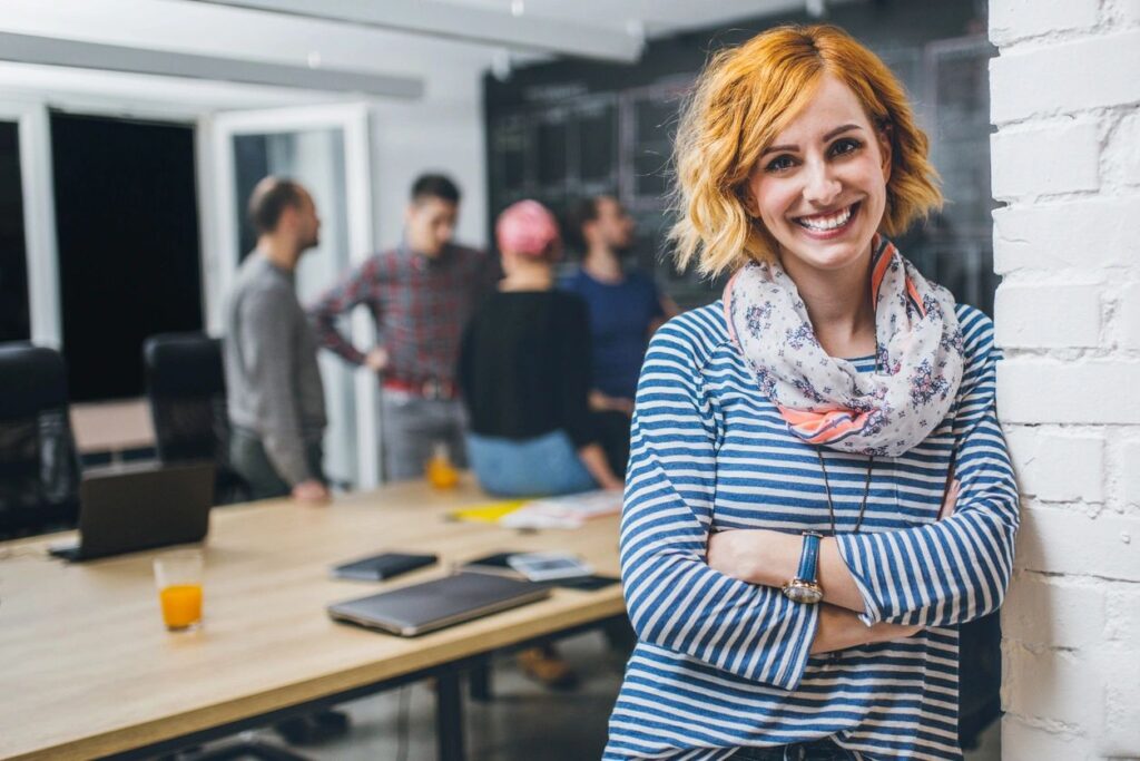 happy coworker smiles at camera while people talk in background