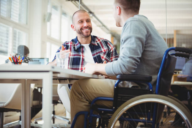 Two men sit at desk, one in wheelchair. | October is Disability Employment Awareness Month